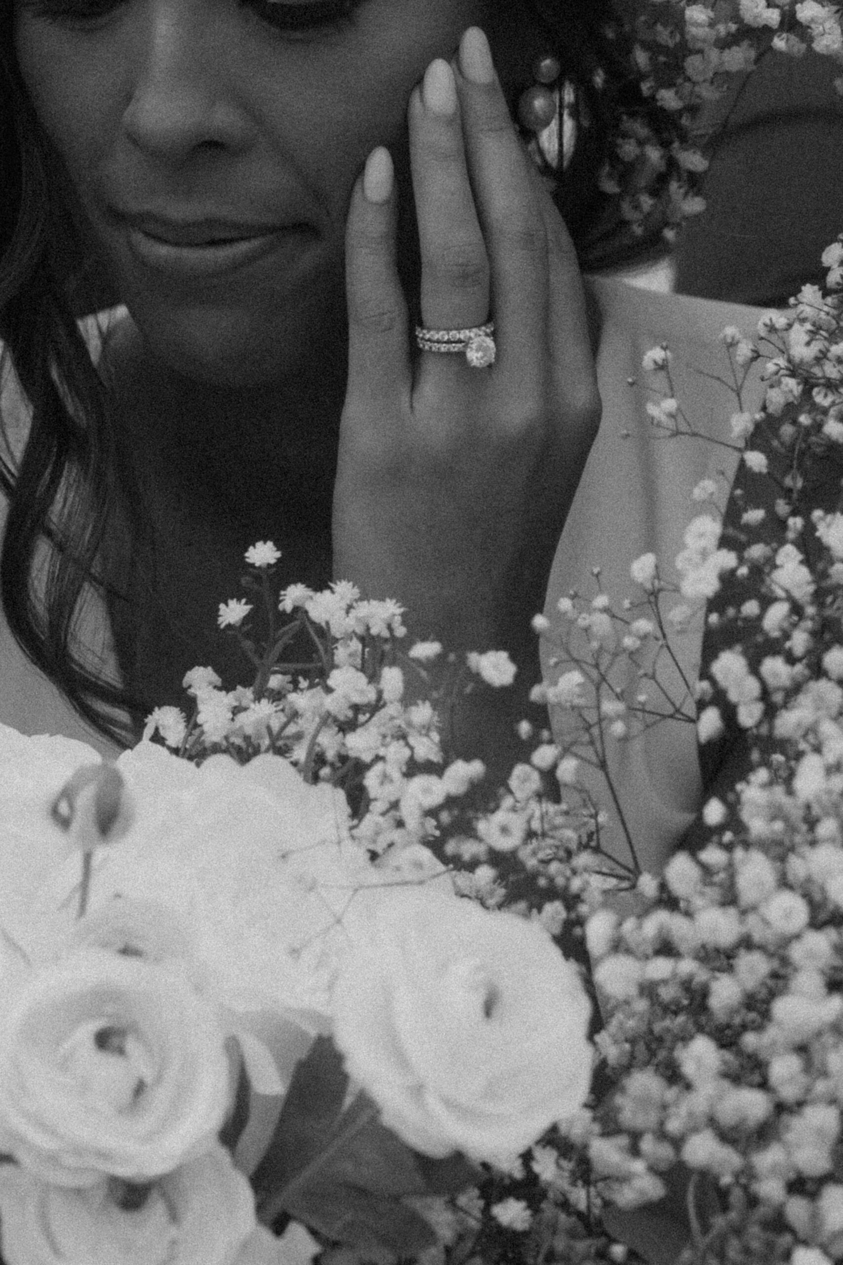 bride surrounded by white flowers showing off ring