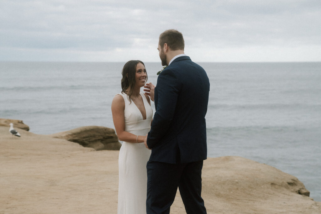 Groom wiping away bride's tears during vow reading on sunset cliffs