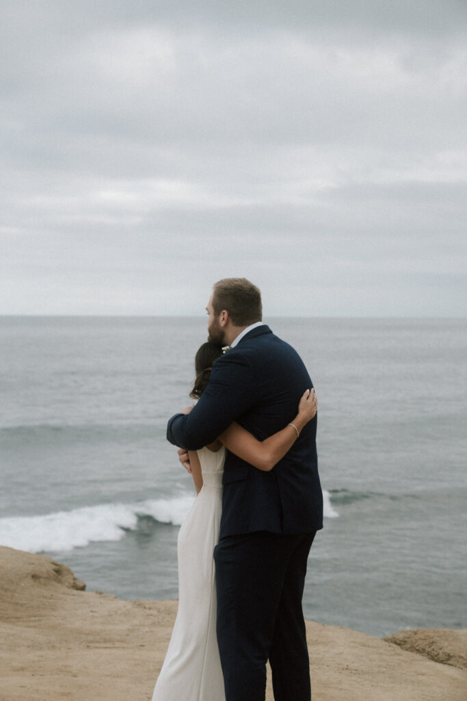 bride and groom embracing on cliff ledge in california