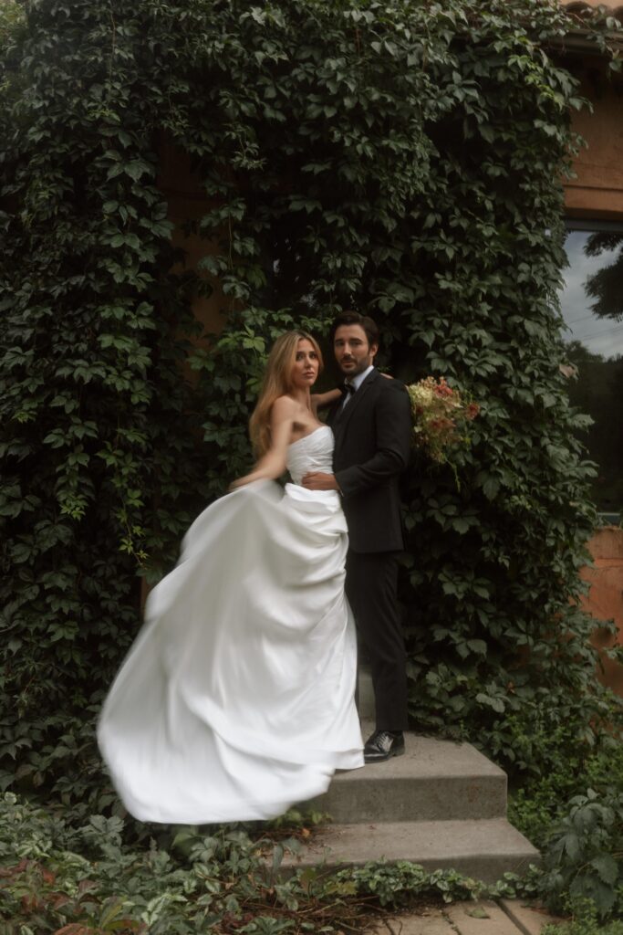 Newlyweds standing in front of a historic Italian villa, surrounded by manicured gardens and timeless architecture, captured in romantic golden hour light