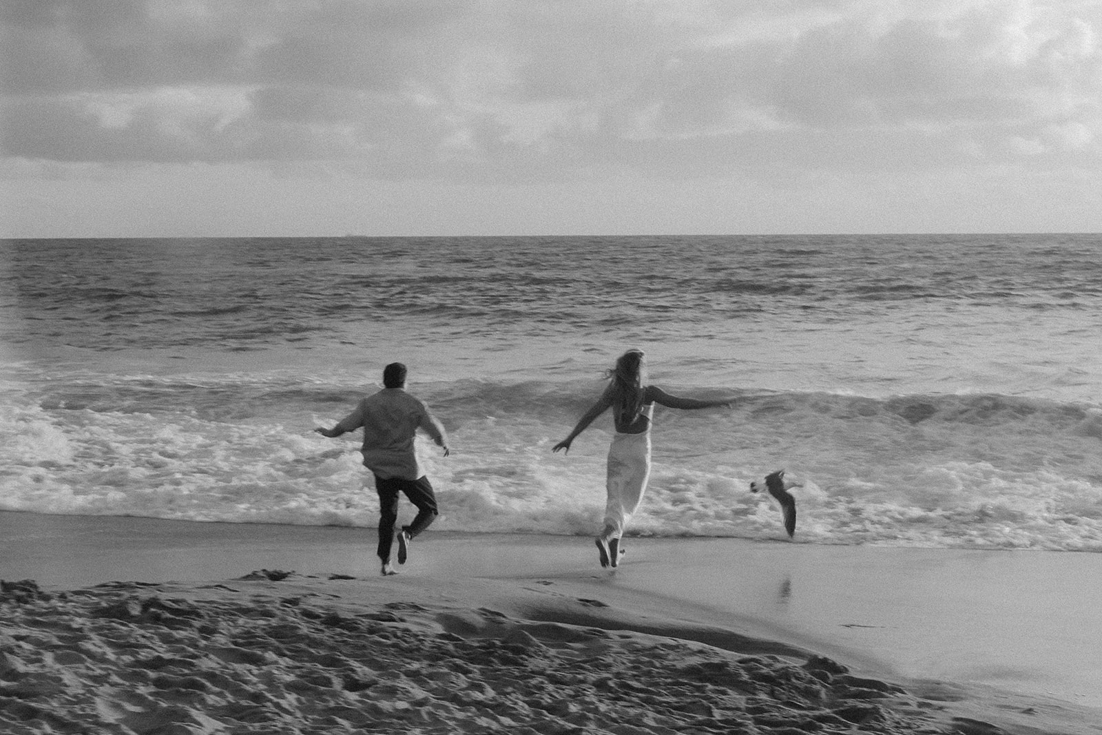 The couple running barefoot along the beach below Heisler Park, laughing as the waves chase their feet and the sun dips low on the horizon.