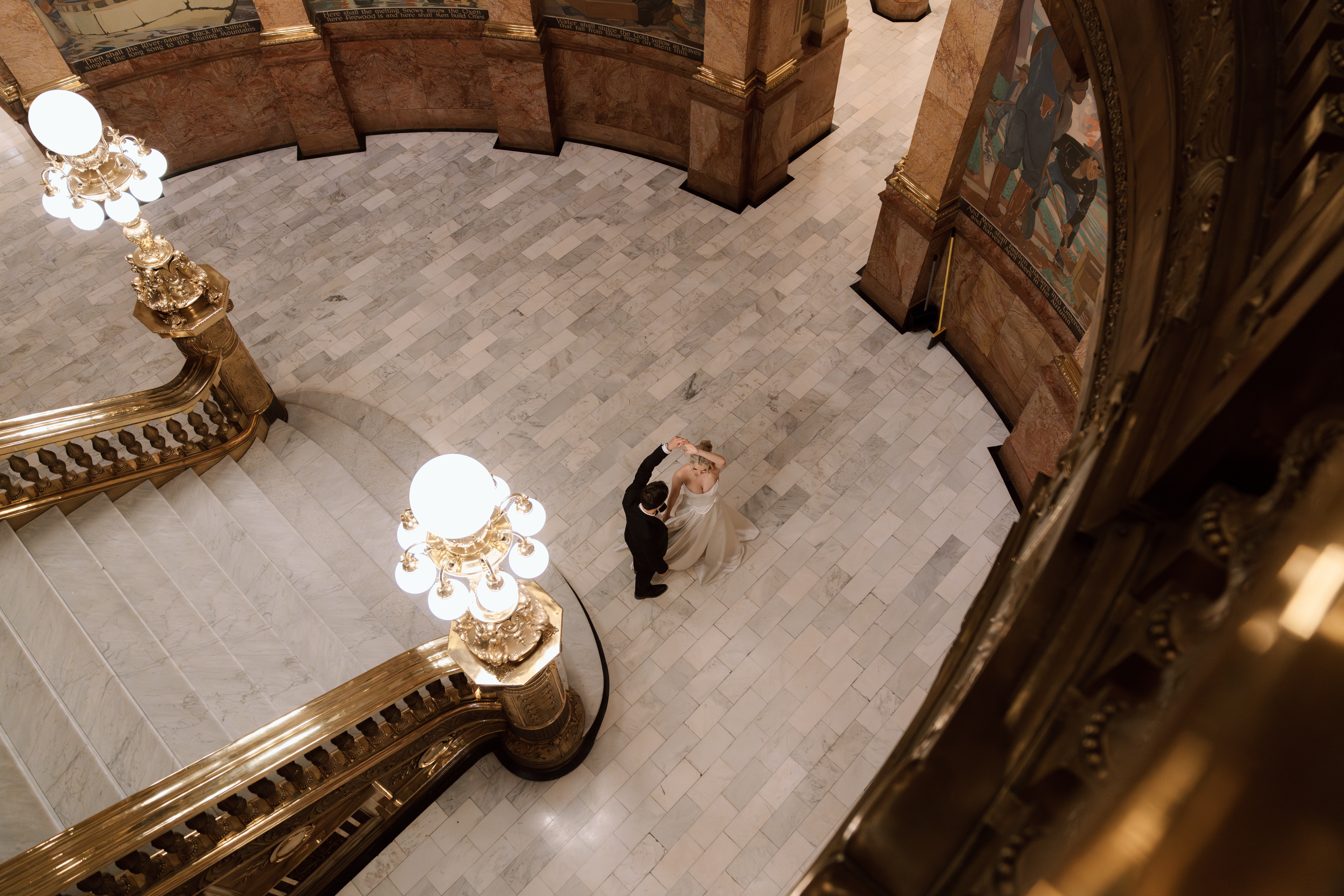 Elegant bride and groom dancing below the grand staircase inside the Denver Capitol Building surrounded by white marble and ornate columns.